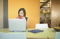 Woman drinking coffee while working on laptop.