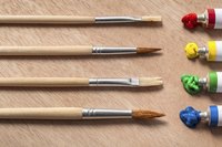 Four paint brushes and paint tubes on a table.