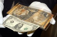 Close-up of a museum curator's hands holding an old silver certficiate next to a modern one dollar bill.