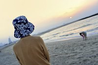 A woman watching her young child and spouse on the beach.