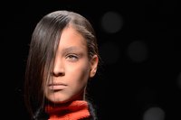 A close up of a model as she walks the runway in a fashion show.