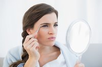 Woman plucking her eyebrows in small hand mirror.