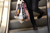 A woman carrying department store shopping bags down the escalator in a mall.