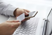 A man is holding a credit card by his phone and laptop.