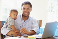 A man smiling at his desk while holding his baby.