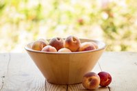 A wooden bowl of peaches on an outdoor table in the summertime.