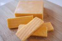 Block and slices of cheddar cheese on a bamboo cutting board.