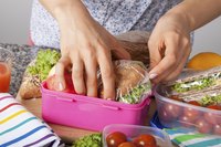 A woman packing lunches into plastic food containers.