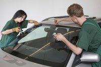 Two professional auto glass installers replace a car windshield.