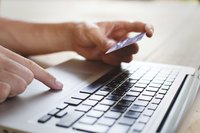 A close-up of a person shopping online with a computer key pad and a credit card.