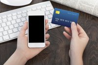 Woman holding credit card beside phone and keyboard