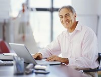 Elderly man researching on laptop in home office.
