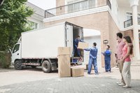 Couple watching movers unload boxes from truck.