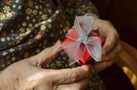 A close-up of an elderly woman holding a small red gift box.