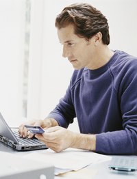 Close-up of a man holding a credit card while typing on a laptop.
