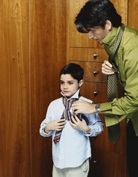 Tying a necktie is an imposing task for a young boy.