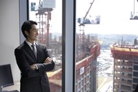 A businessman is looking out the window at construction going on.