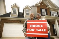 Couple with a "for sale" sign in front of a house.