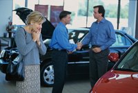 A salesman making a deal with two happy customers at a car dealership.