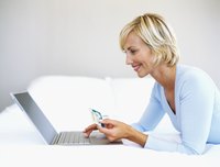 Woman holding up a credit card and working on a laptop.