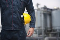 A man is standing with a yellow hard hat in his arms.
