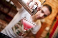 Bartender pouring shaker into mixed drink glass