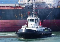 A tug boat dwarfed by the ship it is pulling