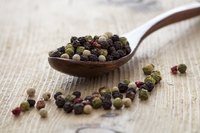 A spoonful of colorful peppercorns on wood.