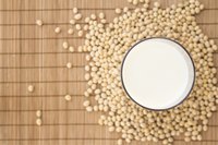 A cup of soy milk surrounded by loose soybeans.