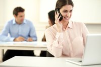 Image of a woman wearing a dress shirt working on her computer and phone.