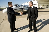 Two businessmen shaking hands in front of a commercial jet.