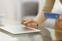 A close-up of a woman shopping online using a tablet computer and a credit card.