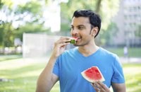 A man eating a slice of watermelon in a city park.