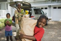 Boy carrying a bag of groceries in front of his family and car.