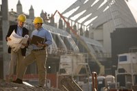 Two architects at a construction site look at blueprints