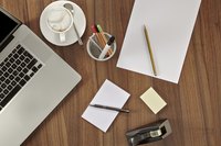 A desk is organized with a lap top, stationary and notepads all in their individual places, spaced out evenly across the desk.