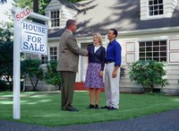 Couple in front of a house with a sold sign shaking realtor's hand
