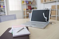 A close-up of a purchse order tablet and laptop with headset on the desk of a small business owner.