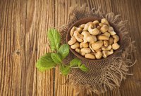 A wood bowl filled with cashews on a table.