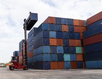 A forklift places a cargo container on top of a stack of other containers