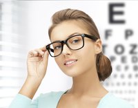 Young adult woman with glasses stands in front of a vision chart