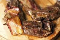 Braised wild beaver meat with bacon on a cutting board.