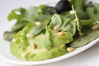A spinach salad rich in Vitamin E topped with avocado slices and pine nuts on white linen.