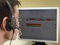 A close-up of an employee speaking into a headset while looking at data on a computer screen.