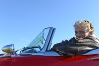 A man in a red leather type jacket in his red sports car.