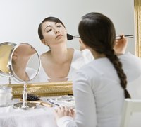 Woman applying makeup in large mirror.
