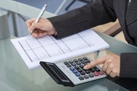 Close-up of woman working on taxes at table with calculator.