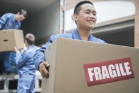 Movers unloading moving truck. One mover carrying box that says fragile.
