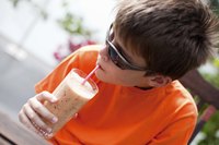 A boy drinking a smoothie at an outdoor table.