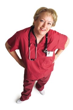 an older caucasian female nurse dressed in pink scubs places her hands on her hips and looks up at the camera